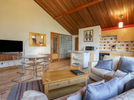 An open-plan living room with cream sofas, a wooden coffee table, glass dining table with chairs, and a kitchen area at Studio Cottage in Surlingham near Poringland