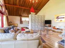 A living room with cream sofas a glass dining table and wooden ceiling at Studio Cottage in Surlingham near Poringland