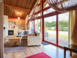 A living room with sofas and cushions next to a wooden coffee table and large red framed glass doors at Studio Cottage in Surlingham near Poringland