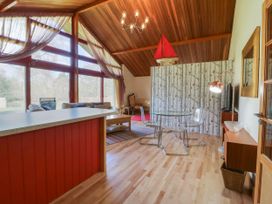A living room with glass dining table clear chairs red kitchen island and large windows at Studio Cottage in Surlingham near Poringland