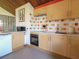 A kitchen with wooden cabinets a black oven a microwave a kettle and colorful tiled backsplash at Studio Cottage in Surlingham near Poringland