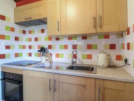A kitchen with wooden cabinets a sink a stovetop a kettle and colorful square tiles on the walls at Studio Cottage in Surlingham near Poringland