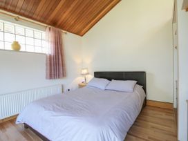 A bedroom with a bed two pillows a nightstand with a lamp a window with curtains and a wooden ceiling at Studio Cottage Surlingham near Poringland