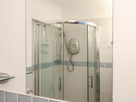 A shower cubicle with glass doors and a wall-mounted electric shower at Studio Cottage in Surlingham near Poringland
