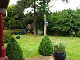 A backyard with a slide attached to a playhouse basketball hoop on a tree and potted plants at Studio Cottage in Surlingham near Poringland