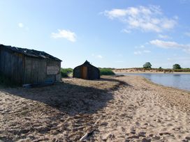 A beach with wooden sheds and a riverbank at Seafield Granary Alnmouth