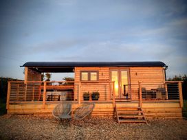 A wooden cabin with a deck and chairs at Fir Tree Shepherd's Hut Llanon