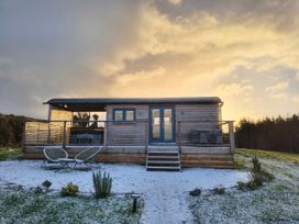 A wooden hut with chairs on a deck at Fir Tree Shepherd's Hut in Llanon