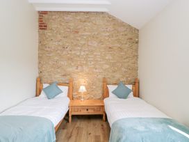 A bedroom with two single beds a wooden nightstand with a lamp and a stone feature wall at South Barn Cottage in Hatford near Stanford In The Vale