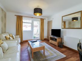 A living room with white leather sofas wooden coffee table and TV stand a mirror on the wall and a glass door at Garden Cottage in Surlingham near Poringland