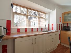 A kitchen with a wooden countertop red and white tiled walls a stainless steel sink a microwave and a kettle at Garden Cottage in Surlingham near Poringland