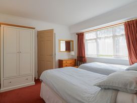 A bedroom with two beds, a wardrobe, a dresser with a lamp, a chair, and a window with curtains at Garden Cottage in Surlingham near Poringland