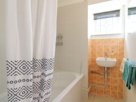A bathroom with a bathtub with a shower curtain a small sink with soap and towels hanging at Garden Cottage in Surlingham near Poringland
