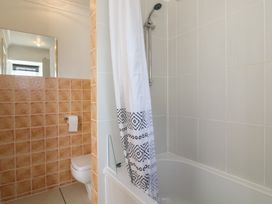 A bathroom with a toilet and bathtub with shower and a curtain with black patterns at Garden Cottage in Surlingham near Poringland