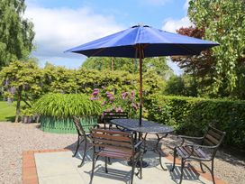 An outdoor patio with a metal table and chairs under a blue umbrella surrounded by greenery and flowers at Garden Cottage in Surlingham near Poringland