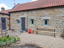 An exterior stone wall of a building with a blue door and windows a wooden bench a small wooden stool a red child size chair and garden decorations at Wayside Farm Dairy Cottage Cloughton near Burniston