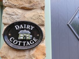 A sign reading Dairy Cottage mounted on a stone wall next to a gray door with a diamond-shaped window at Wayside Farm Dairy Cottage Cloughton near Burniston