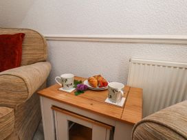 A wooden side table with two animal print mugs, a plate with croissants and strawberries, flowers between two fabric armchairs at Wayside Farm Dairy Cottage Cloughton near Burniston