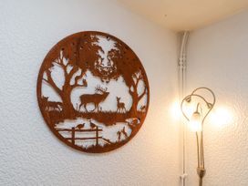 A metal wall art depicting deer and birds next to a floor lamp in a corner of a room at Wayside Farm Dairy Cottage in Cloughton near Burniston