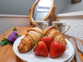 A plate with croissants and strawberries on a wooden table with two mugs and a mirror at Wayside Farm Dairy Cottage in Cloughton near Burniston