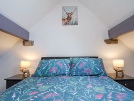 A bedroom with a bed with floral bedding two bedside tables with lamps and small animal figurines and a deer painting on the wall at Wayside Farm Dairy Cottage in Cloughton near Burniston