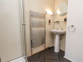 A bathroom with a shower, towel rack, pedestal sink, mirror, and soap dispenser at Wayside Farm Dairy Cottage in Cloughton near Burniston