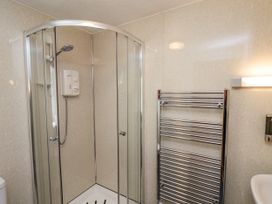 A corner shower enclosure with glass doors a chrome towel radiator a soap dispenser and a white sink at Wayside Farm Dairy Cottage in Cloughton near Burniston