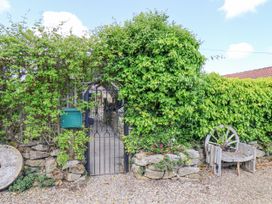 An outdoor iron gate surrounded by greenery with a mailbox on the left and a wooden bench made from a wagon wheel on the right at Wayside Farm Dairy Cottage in Cloughton near Burniston