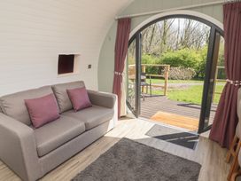 A seating area with a sofa and purple pillows next to a large arched glass door opening to a deck and garden at The Rowan Pod in Cowbridge