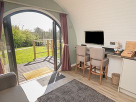 A room with an arched glass door leading outside two chairs at a counter with a mounted television and coffee mugs at The Rowan Pod in Cowbridge