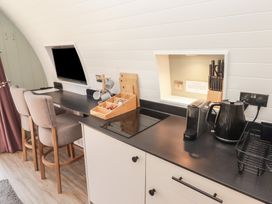 A kitchen counter with a kettle coffee machine knife block and stools next to a wall mounted TV at The Rowan Pod in Cowbridge