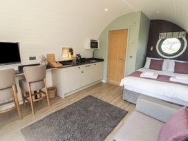 A small room with a kitchen area dining chairs bed and a round window at The Rowan Pod in Cowbridge