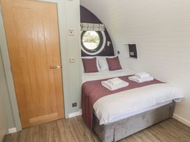 A bedroom with a double bed pillows and towels on the bed a round window and a wooden door at The Rowan Pod in Cowbridge