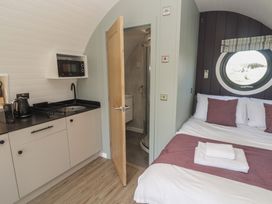 A small room with a kitchenette and bed next to a bathroom with an open door at The Rowan Pod in Cowbridge