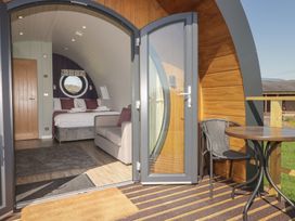 A bedroom with a double bed and sofa visible through an open door leading to a patio with a table and chair at The Rowan Pod in Cowbridge