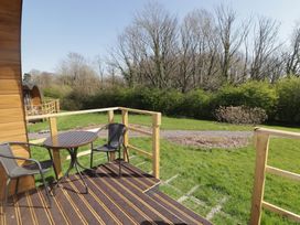 A small wooden deck with two black chairs and a round table overlooking grass and trees at The Rowan Pod in Cowbridge