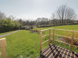 A grassy garden with a gravel path wooden railings and leafless trees at The Rowan Pod in Cowbridge