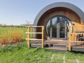 A small round wooden pod with a deck and outdoor chairs in a grassy field at The Rowan Pod in Cowbridge
