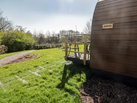 A wooden pod with a small deck and chairs on grass with a gravel path and trees at The Rowan Pod in Cowbridge