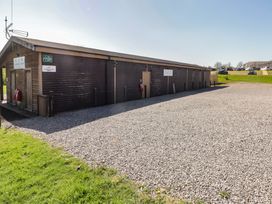A gravel parking area next to a long wooden cabin building with signs and a grass patch at The Rowan Pod in Cowbridge