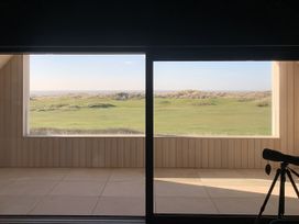 A view of grass and dunes through a large window at Twyn Isaf in Borth
