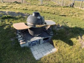 A barbecue grill on a stone base with a wooden table at Twyn Isaf in Borth