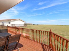 A deck with a table and chairs overlooking a grassy area at Boa Vista in Bacton