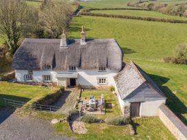 A house with a thatched roof and outdoor seating at Westacombe Farmhouse in Dunsford