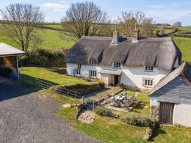 An outdoor area with a thatched roof house and patio furniture at Westacombe Farmhouse in Dunsford