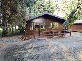 A brown wooden cabin surrounded by trees with a patio and chairs at Pheasant in Withern near Alford
