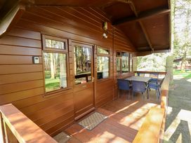 A wooden porch with a table and six chairs outside a cabin in a wooded area at Kestrel Withern near Alford