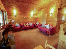 A living room with wooden walls and ceiling with red sofas and armchairs with cushions at Kestrel in Withern near Alford