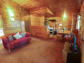 A wooden panelled living room with a red sofa a dining table with chairs a television and a kitchen area at Kestrel in Withern near Alford