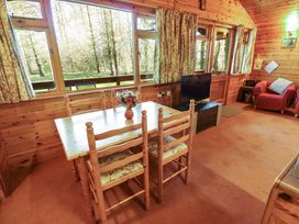 A wooden dining table with four chairs and a vase of flowers a television on a stand two armchairs and windows with floral curtains at Kestrel Withern near Alford